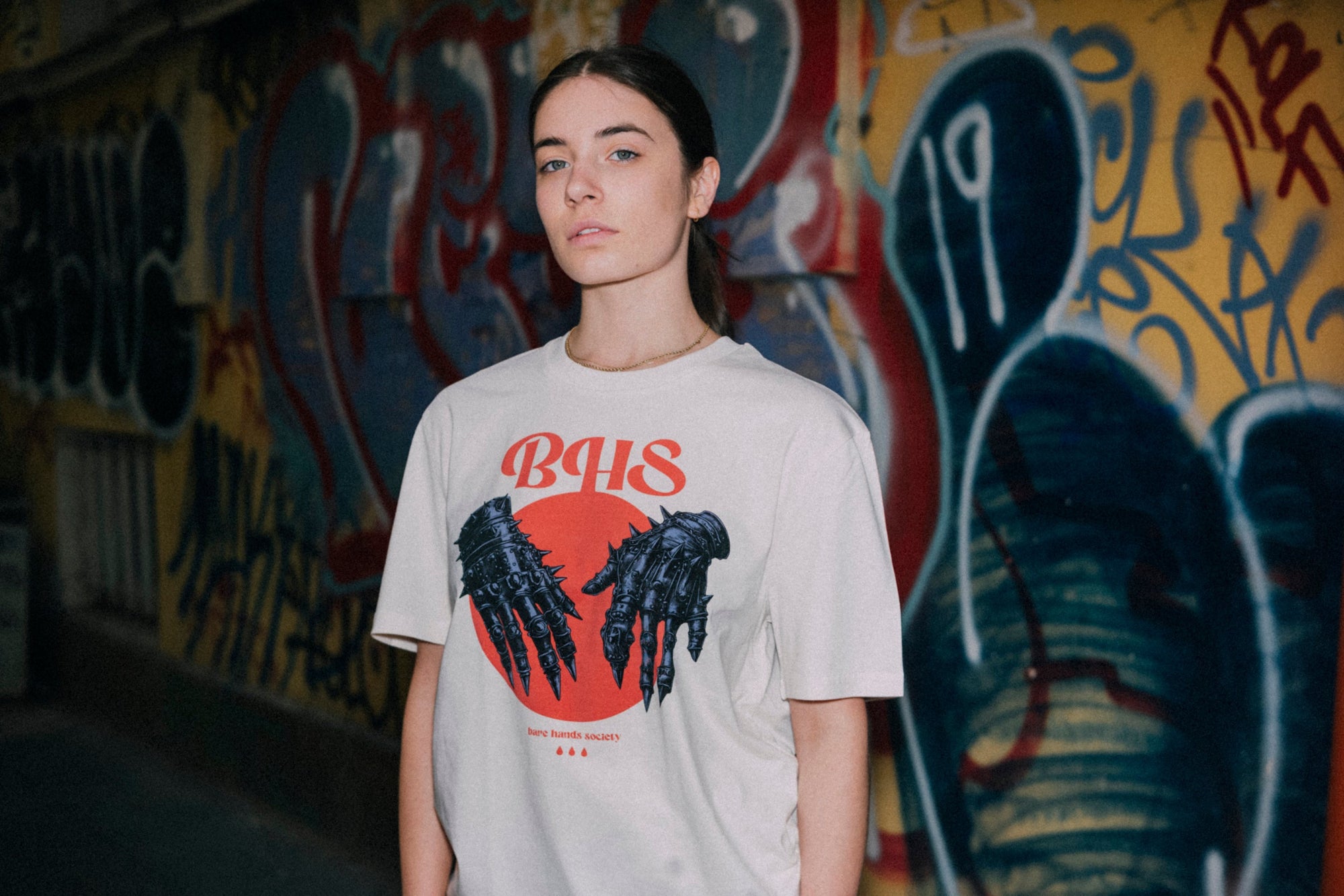 Person wearing a t-shirt with a graphic design in front of a graffiti-covered wall