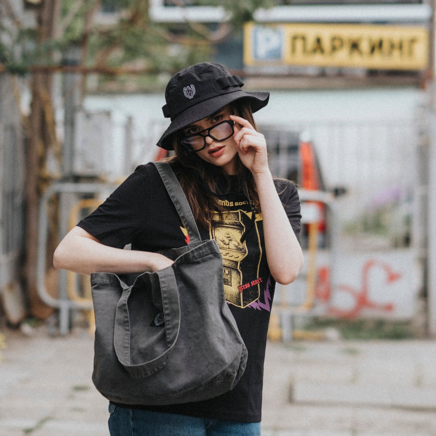 Person holding a gray bag on an urban street with graffiti and a bus stop sign.