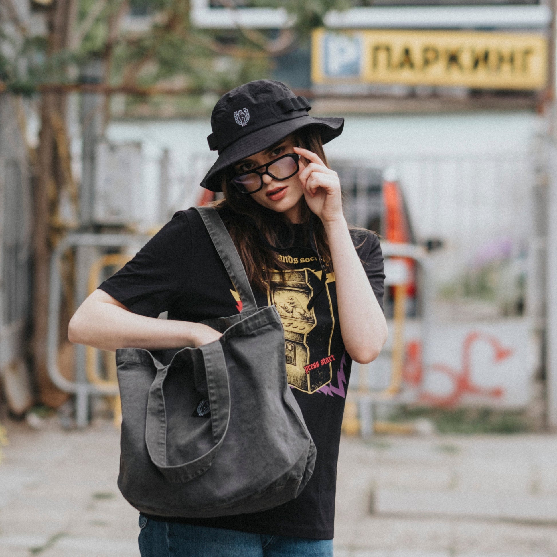 Person holding a gray bag on an urban street with graffiti and a bus stop sign.