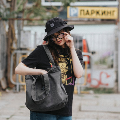 Person holding a gray bag on an urban street with graffiti and a bus stop sign.