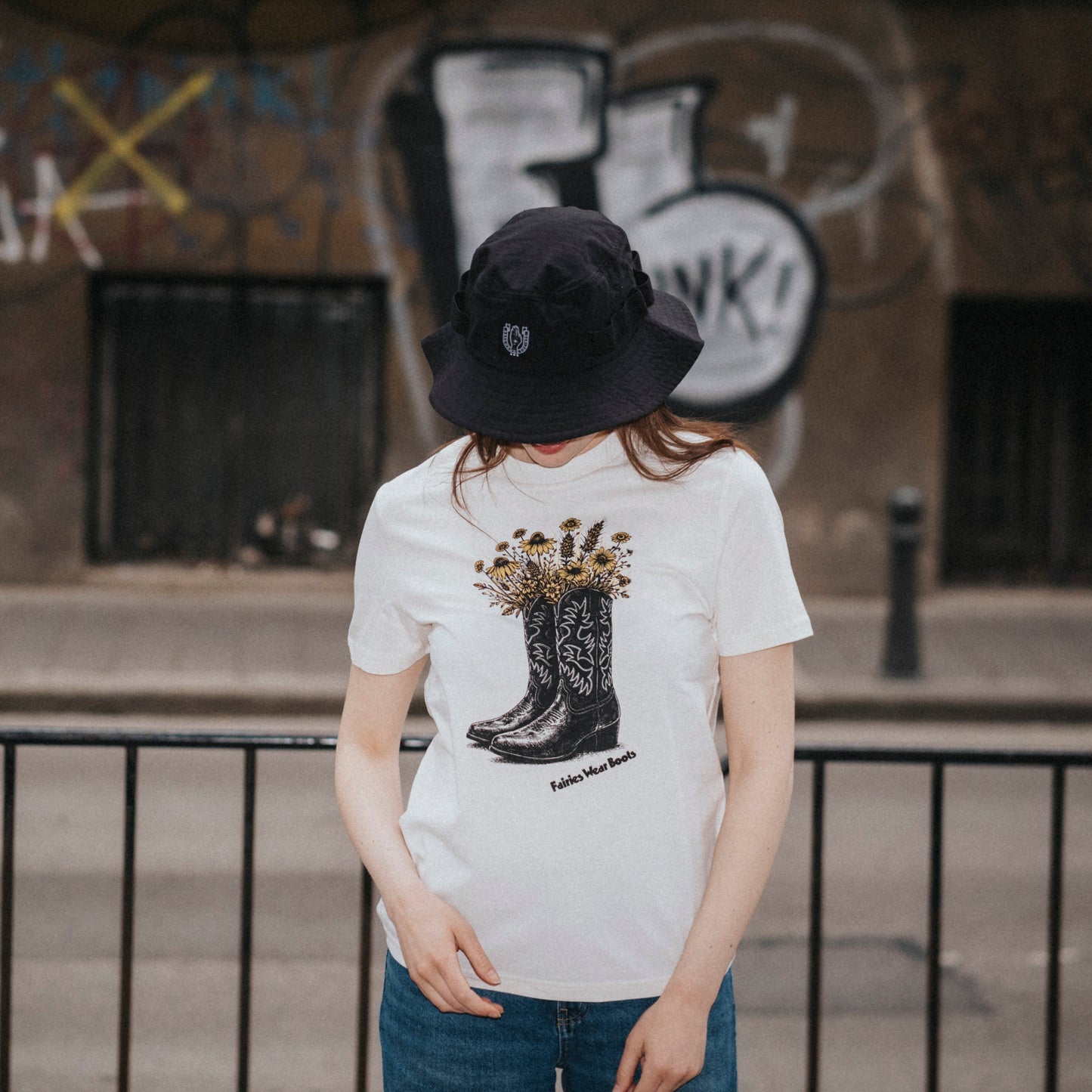 Person wearing a white t-shirt with a graphic design in an urban setting with graffiti.