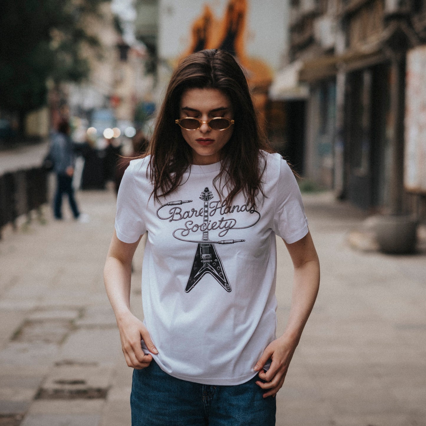 Person wearing a white t-shirt with a guitar design on a city street.