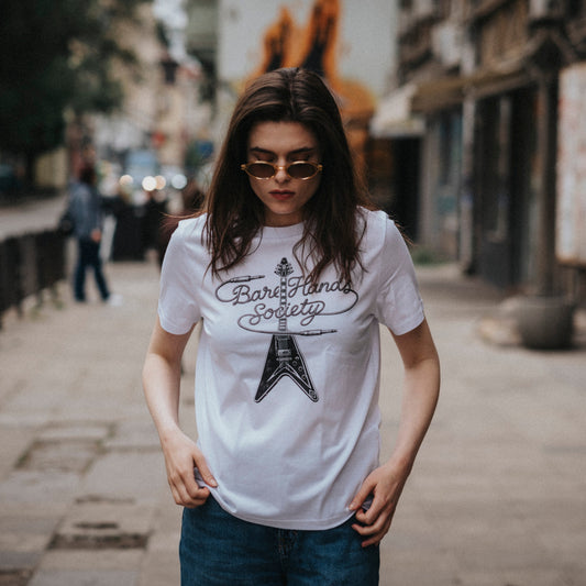 Person wearing a white t-shirt with a guitar design on a city street.