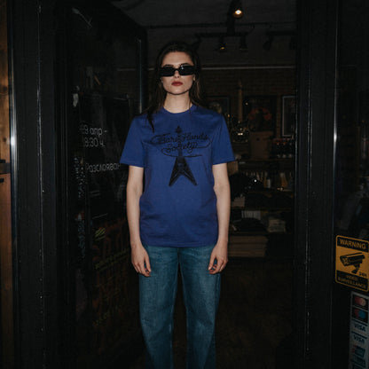 Person wearing a blue t-shirt with a black graphic design in a dark room.